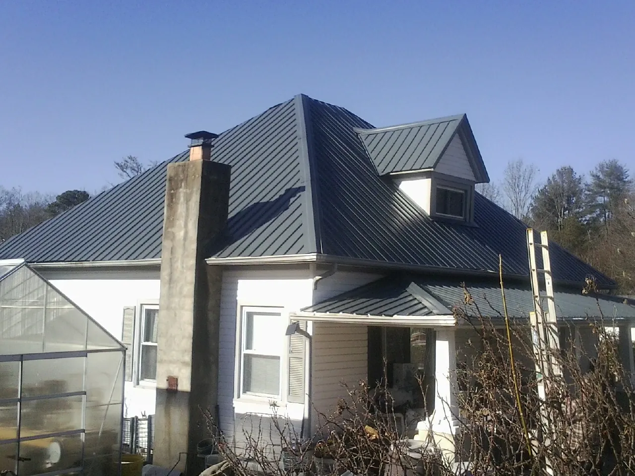 Dark blue standing seam metal roof on a white farmhouse with dormer — Slate & Tile Roof Repair by Roofing Brothers in Harpursville