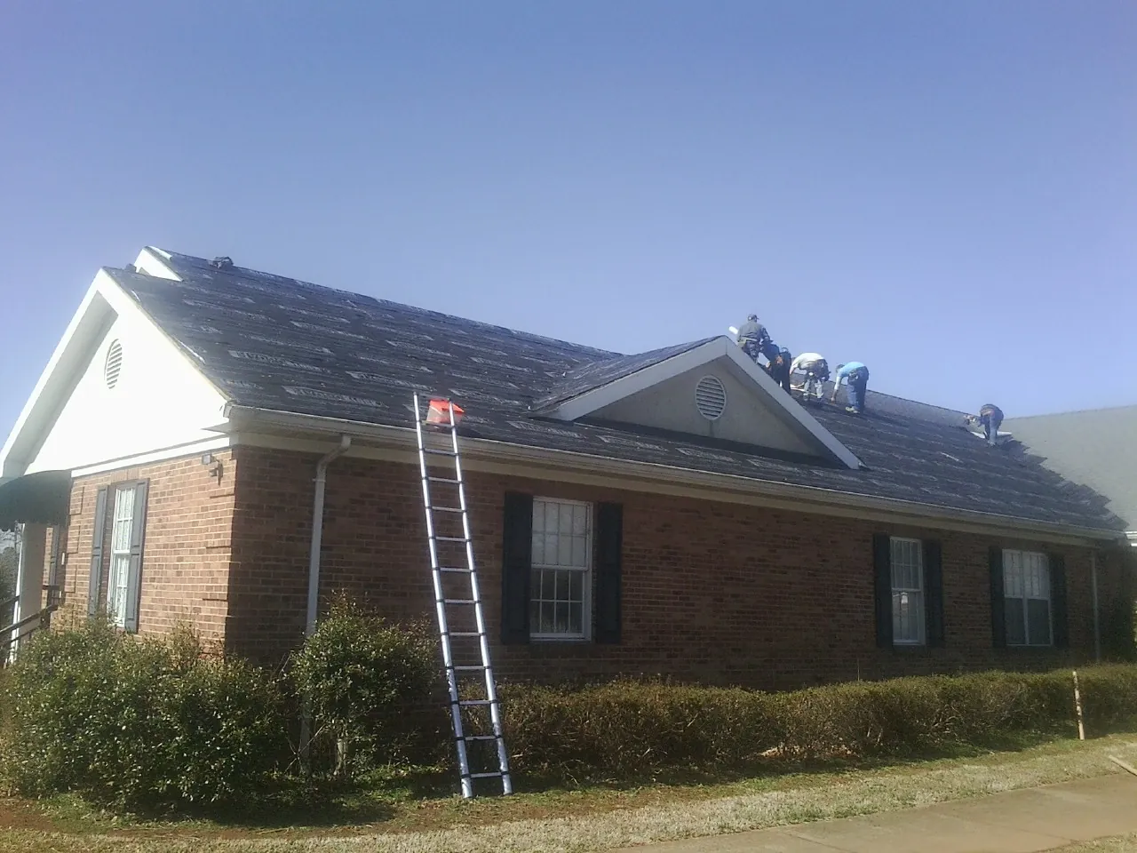 Crew tearing shingles off a brick ranch roof with a ladder set — Metal Roof Repair work by our crew in Harpursville