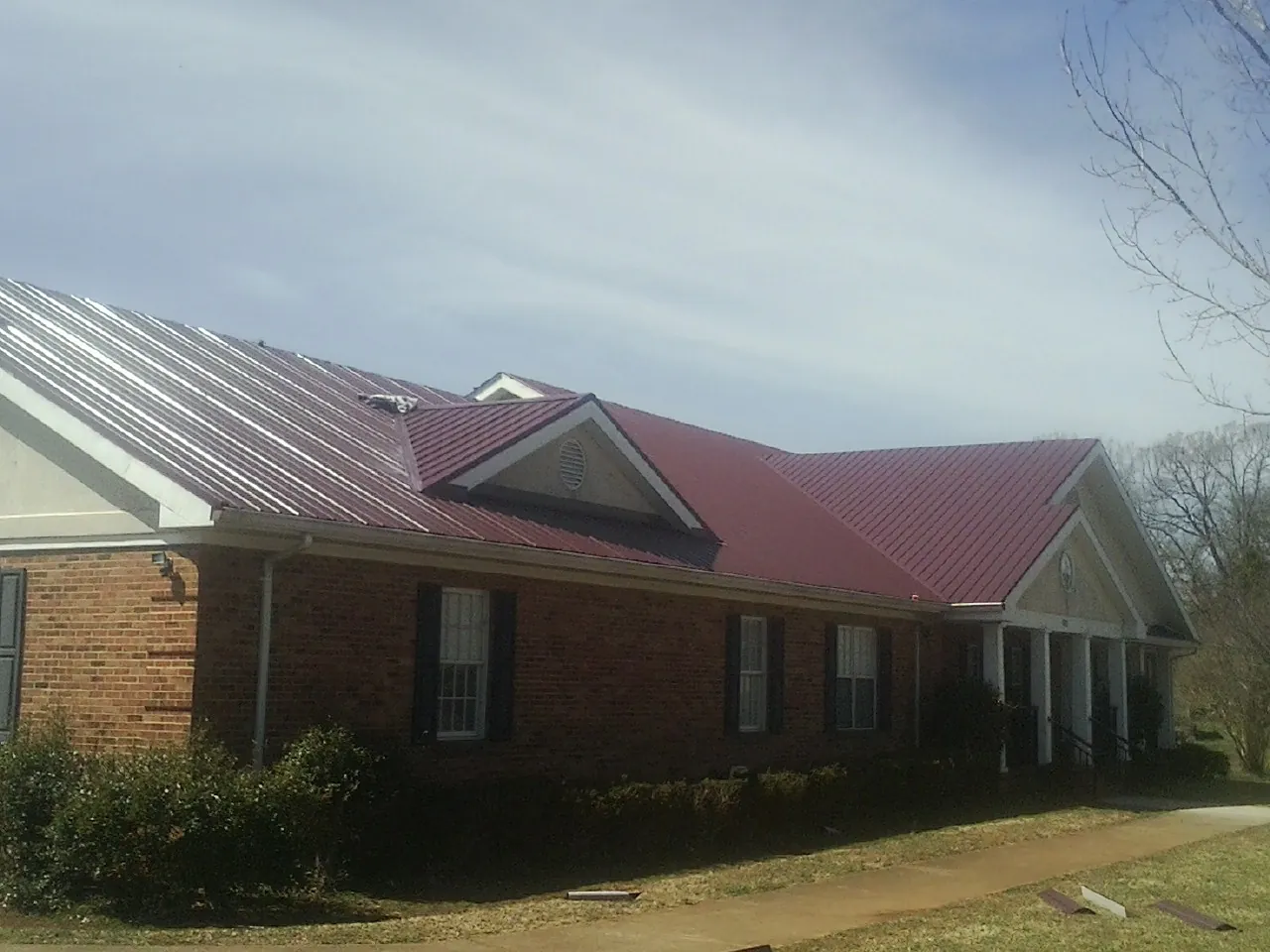 Red metal roof with gabled entries on a long brick building, from a Hail Damage Roof Repair job in Harpursville