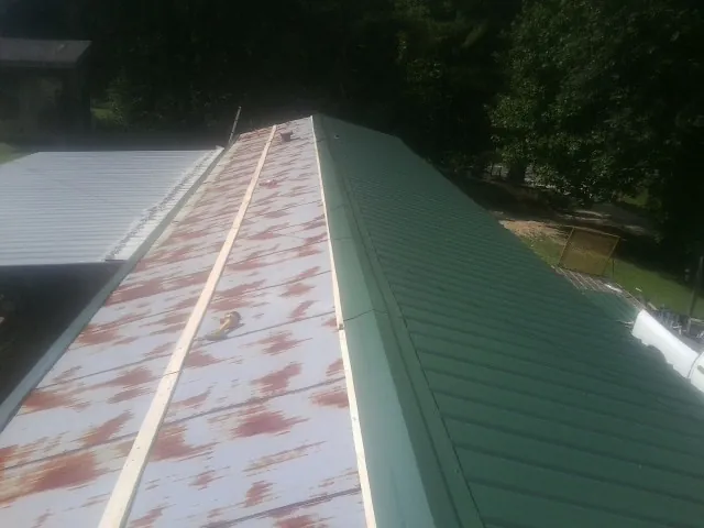 Old rusted panels beside newly installed green metal roofing — Wind Damage Roof Repair by Roofing Brothers in Harpursville