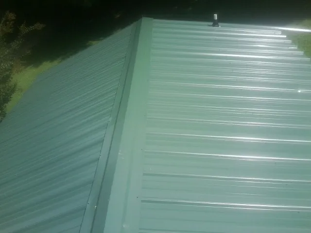New green metal panels meeting at the ridge of a roof — Flat Roof Repair work by our crew in Harpursville