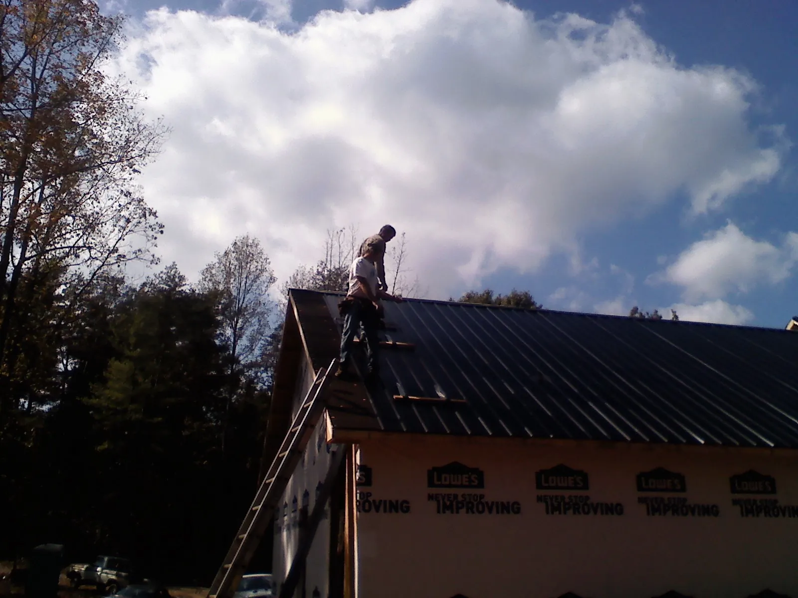 Roofer fastening dark metal panels high against a cloudy sky, from a Roof Inspection job in Harpursville