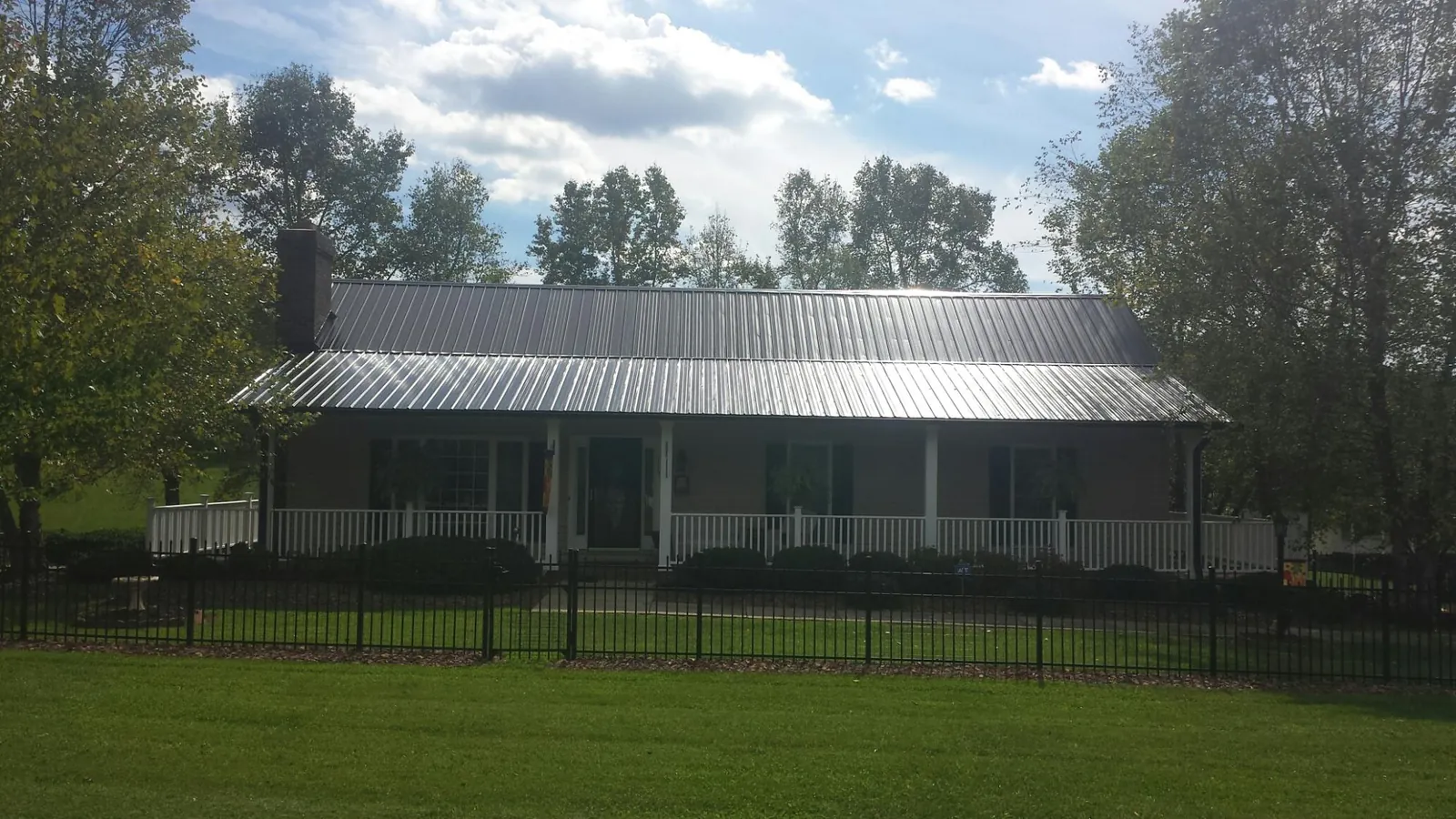 Gray metal roof on a brick ranch with a full width front porch — Gutter Guard Installation work by our crew in Harpursville