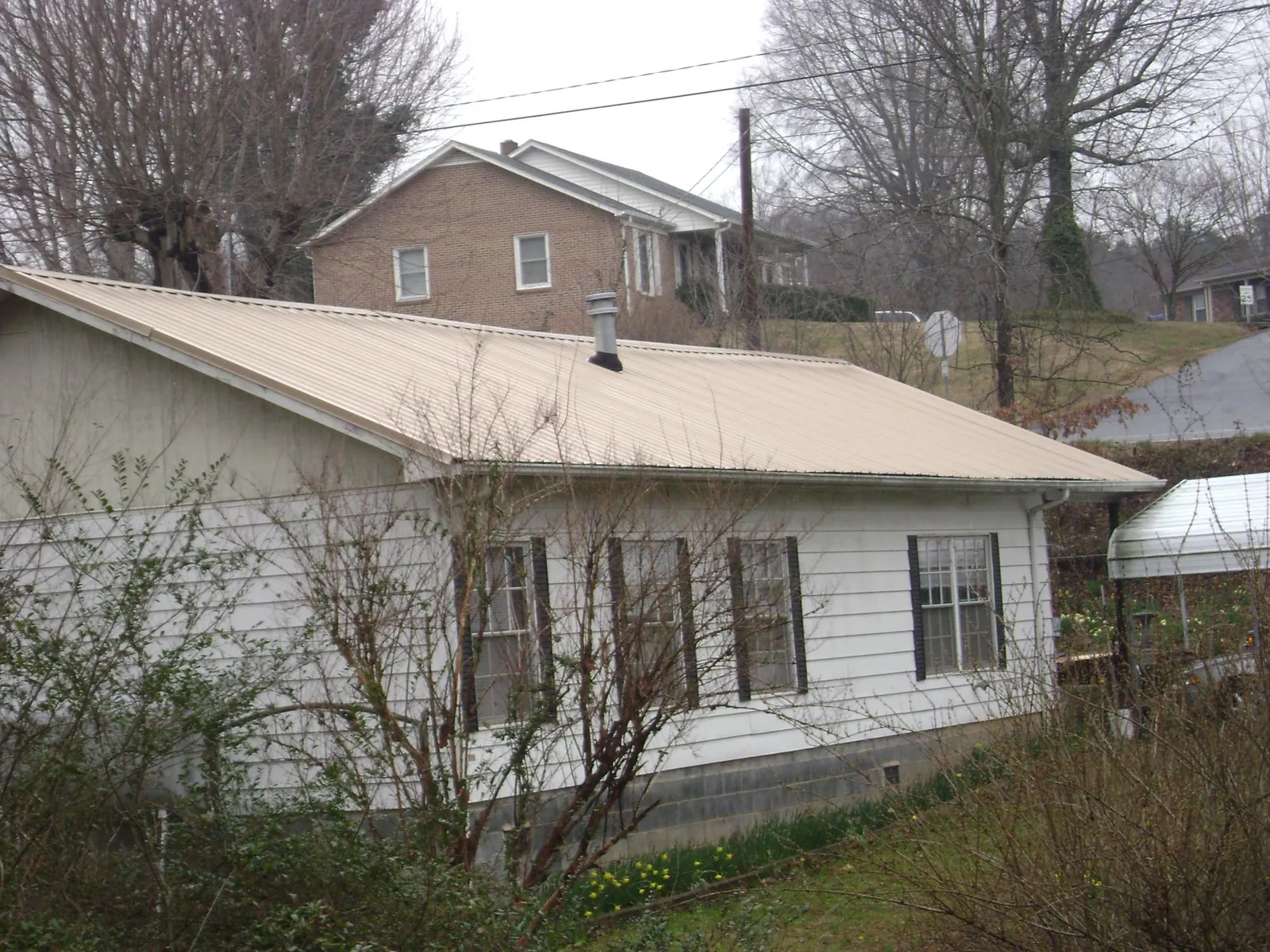 Tan metal roof on a white sided house set into a hillside — Commercial Roofing by Roofing Brothers in Harpursville