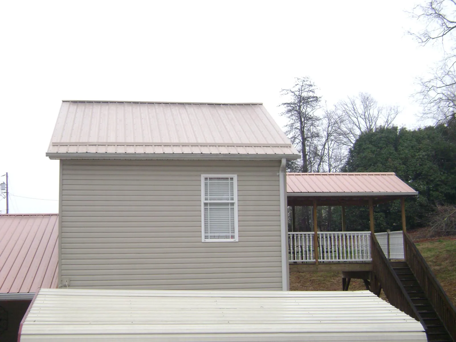 Tan metal roofs on a two story addition and attached porch, from a Roof Replacement job in Harpursville